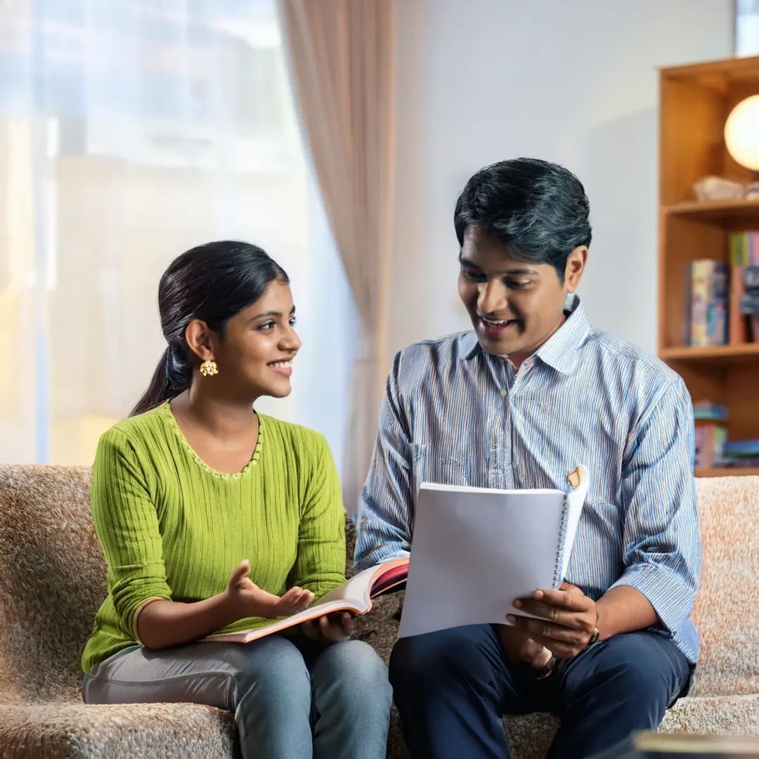 a tutor and student sitting on a couch looking at a book when someone searches Best Home Tutor Bureau in Dwarka