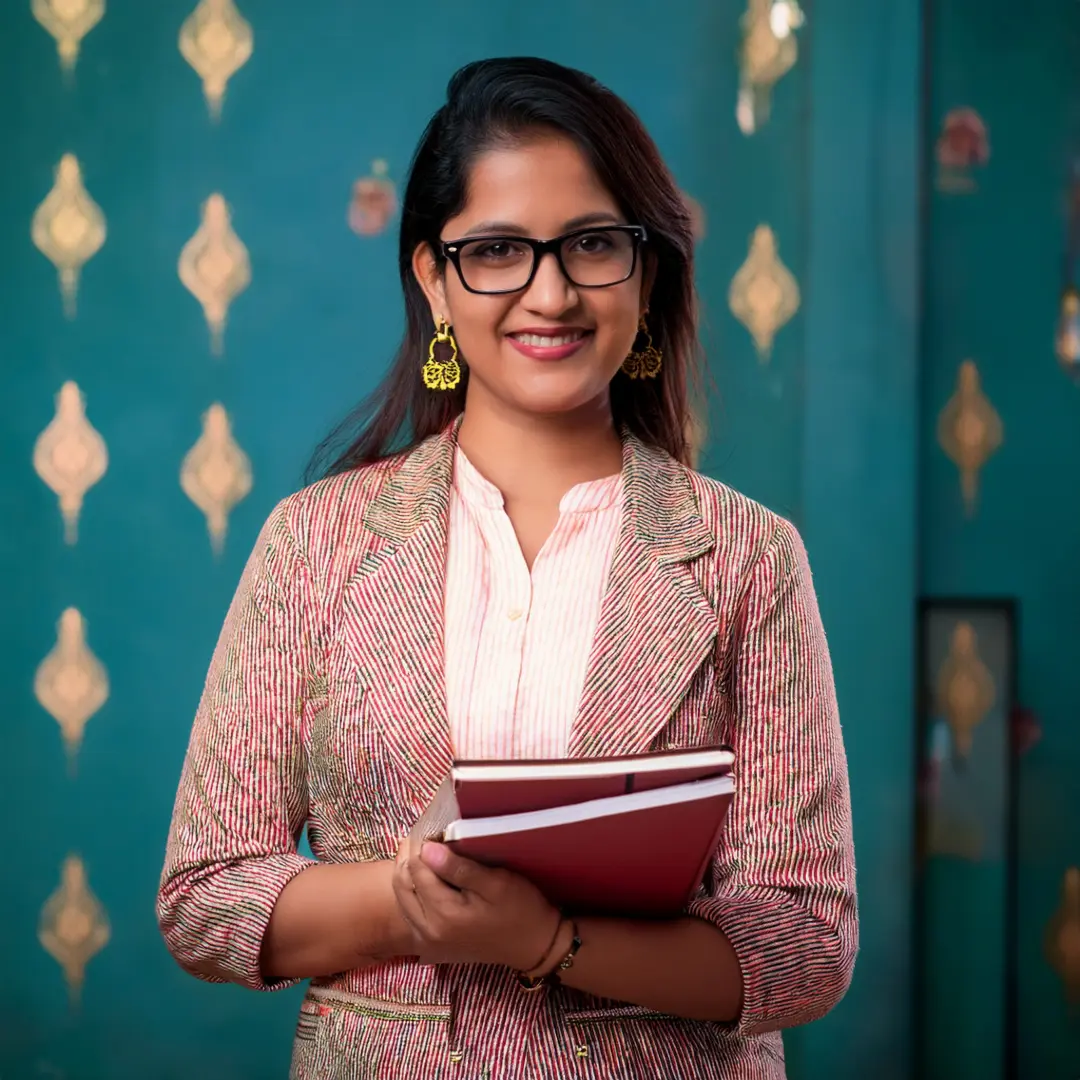 a tutoress who is one of the Best home tutor in West Delhi, holding books in front of a blue wall